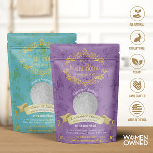 Front-facing product shot of Mom Bomb Coconut Lime and Lavender Honey bath salts standing side by side on a wood counter, with icons indicating all-natural, vegan, cruelty-free, and made in the USA