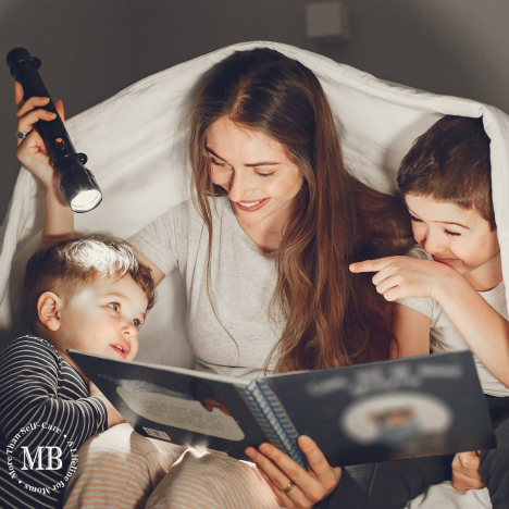 Mother reading a bedtime story under a blanket with two young boys, smiling and holding a flashlight